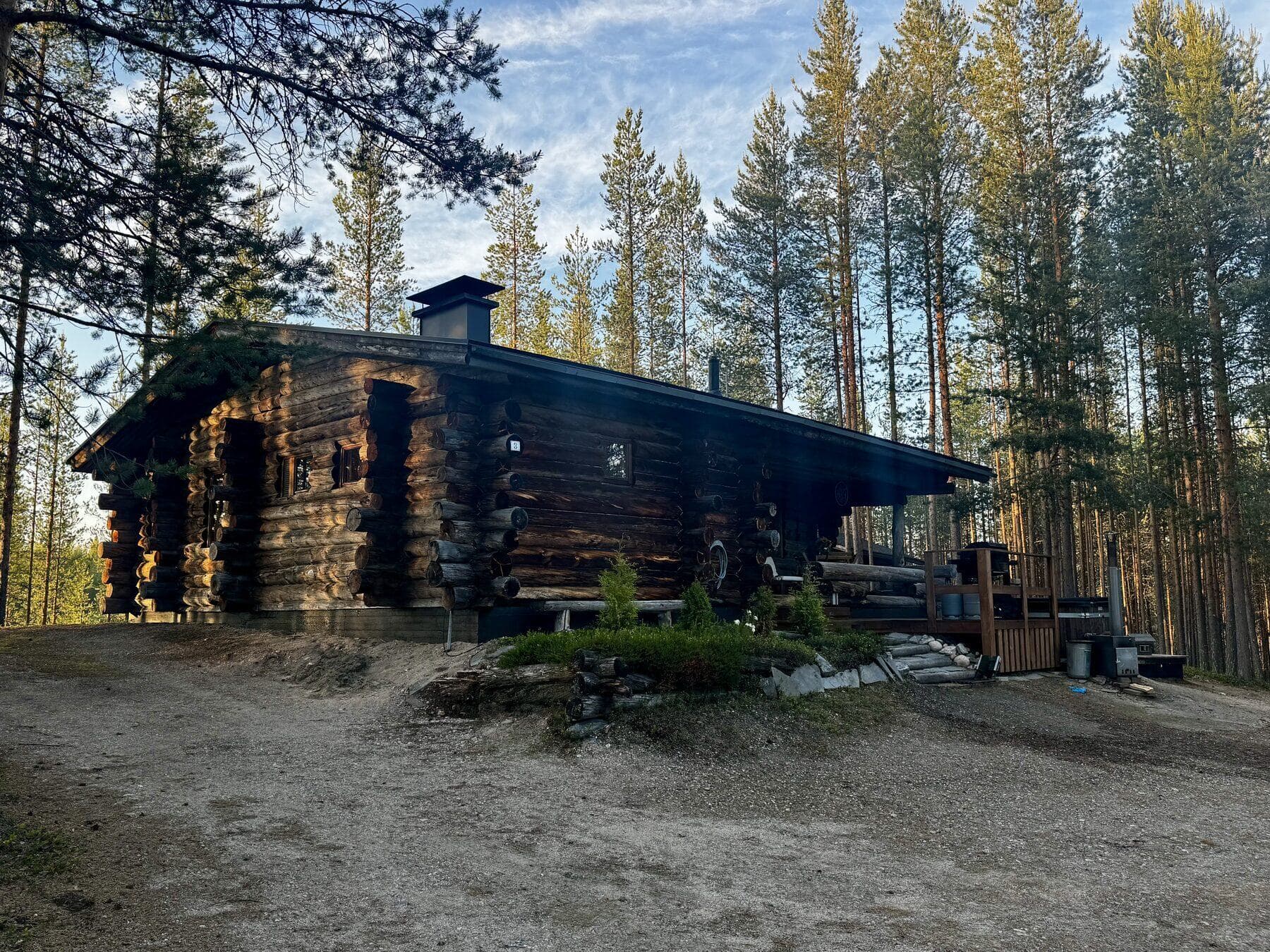 Kelohirsimökki kesäillan valossa mäntyjen keskellä
